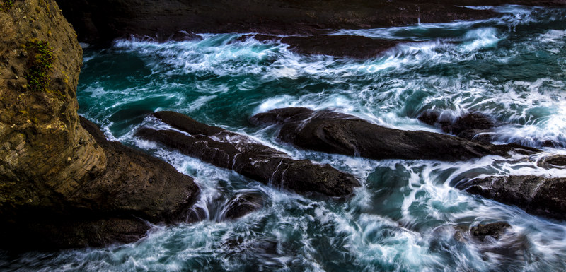 Wide panoramic long exposure of turquoise waves crashing over dark rock formations at Cape Flattery